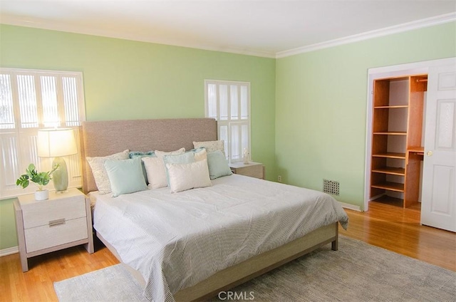 bedroom featuring crown molding, a walk in closet, and light wood-type flooring