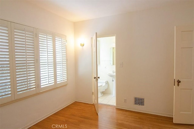 unfurnished bedroom featuring connected bathroom and light wood-type flooring