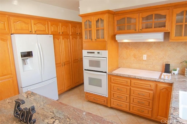 kitchen featuring light tile patterned flooring, light stone counters, backsplash, and white appliances