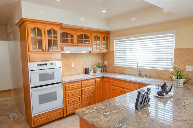 kitchen with double oven, sink, decorative backsplash, light tile patterned floors, and light stone countertops