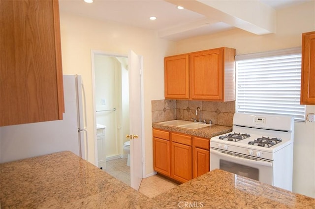 kitchen with tasteful backsplash, sink, white gas range oven, and light tile patterned floors