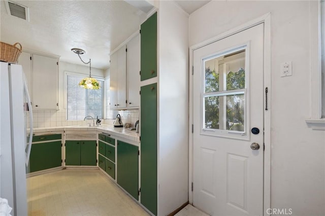 kitchen with backsplash, white fridge, hanging light fixtures, green cabinetry, and white cabinets