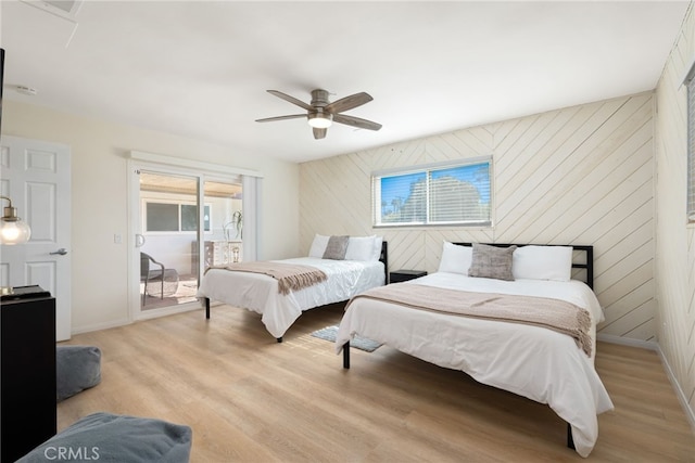 bedroom featuring ceiling fan, access to outside, light wood-type flooring, and wooden walls