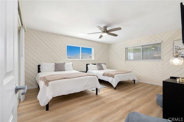 bedroom with ceiling fan, light wood-type flooring, and wooden walls