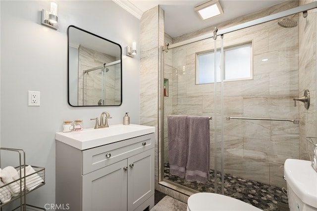 bathroom with toilet, vanity, a shower with door, and ornamental molding