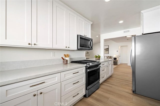 kitchen with appliances with stainless steel finishes, light hardwood / wood-style flooring, and white cabinets