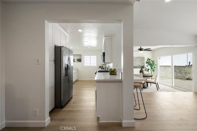 kitchen with appliances with stainless steel finishes, white cabinetry, ceiling fan, a breakfast bar, and light hardwood / wood-style flooring