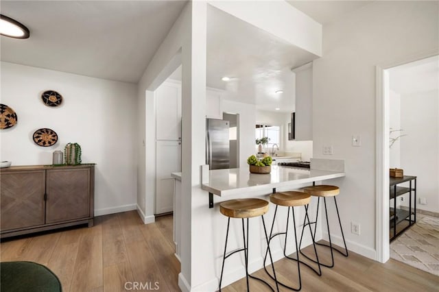 kitchen featuring a kitchen bar, white cabinetry, light hardwood / wood-style floors, kitchen peninsula, and stainless steel refrigerator