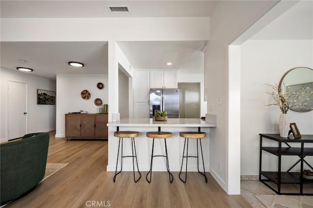 kitchen with white cabinetry, light hardwood / wood-style floors, stainless steel fridge, kitchen peninsula, and a breakfast bar area