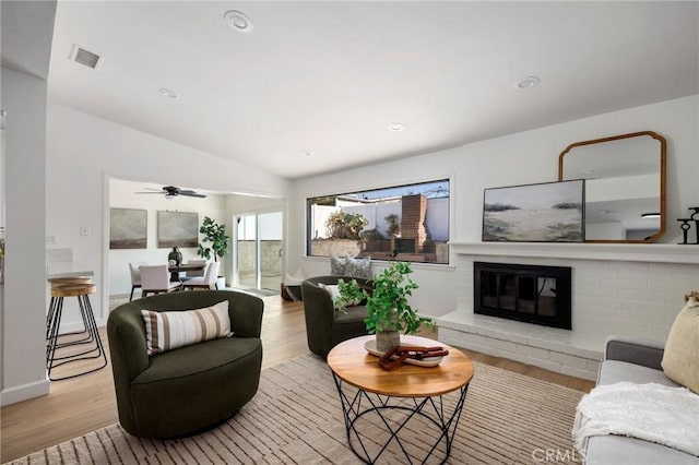 living room featuring a brick fireplace, light hardwood / wood-style floors, lofted ceiling, and ceiling fan