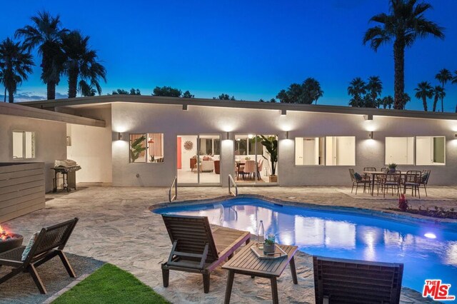 pool at dusk with a patio area and area for grilling