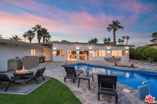 pool at dusk featuring a patio area, grilling area, and a fire pit