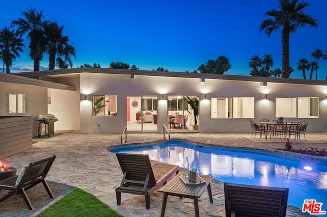 pool at dusk featuring a grill and a patio area