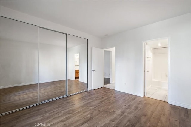 unfurnished bedroom featuring wood-type flooring, connected bathroom, and a closet