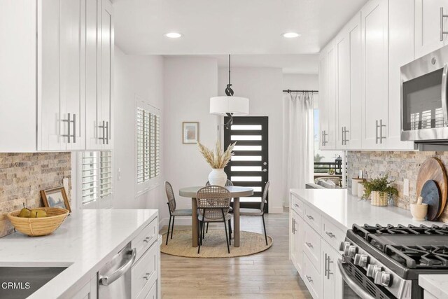 kitchen with decorative light fixtures, decorative backsplash, white cabinets, and stainless steel appliances