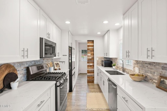 kitchen with decorative backsplash, sink, white cabinetry, light stone countertops, and stainless steel appliances