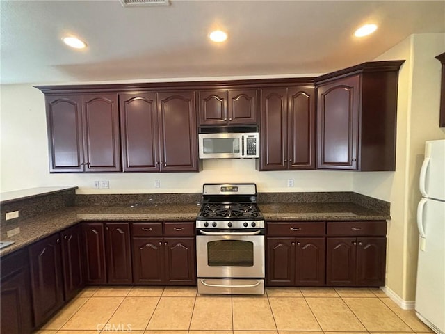 kitchen featuring light tile patterned floors, appliances with stainless steel finishes, and dark stone countertops