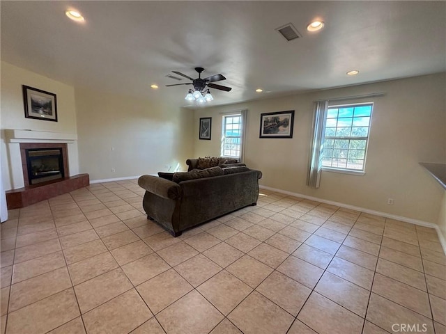 living room featuring ceiling fan, light tile patterned flooring, a fireplace, and a wealth of natural light