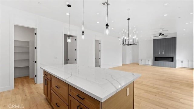 kitchen featuring a large fireplace, hanging light fixtures, a large island, light stone counters, and ceiling fan with notable chandelier