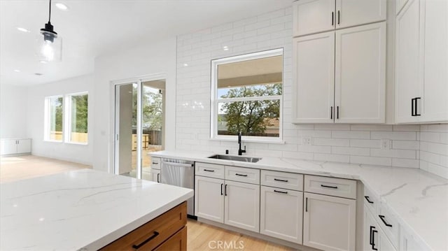 kitchen featuring decorative light fixtures, dishwasher, sink, light stone countertops, and white cabinets