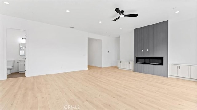 unfurnished living room with ceiling fan, a large fireplace, and light hardwood / wood-style floors