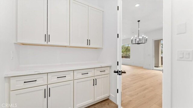 interior space with light wood-type flooring, light stone countertops, a chandelier, pendant lighting, and white cabinets