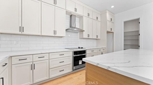 kitchen with white cabinetry, black electric stovetop, oven, wall chimney exhaust hood, and light stone counters