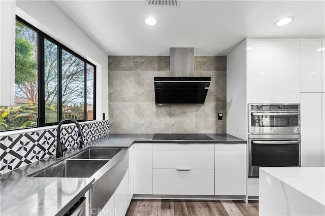 kitchen featuring dark stone countertops, white cabinets, black electric stovetop, and range hood