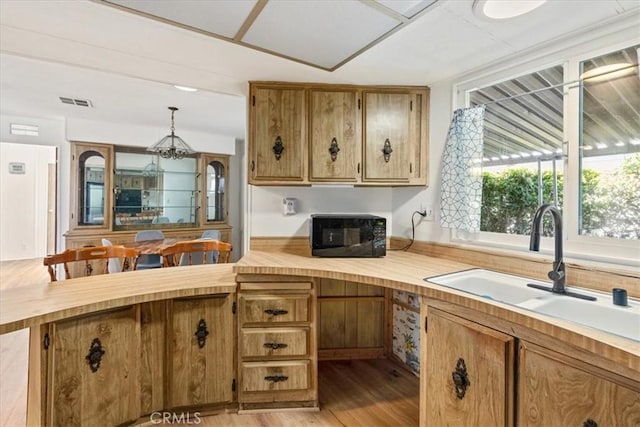 kitchen with visible vents, brown cabinetry, a peninsula, black microwave, and a sink