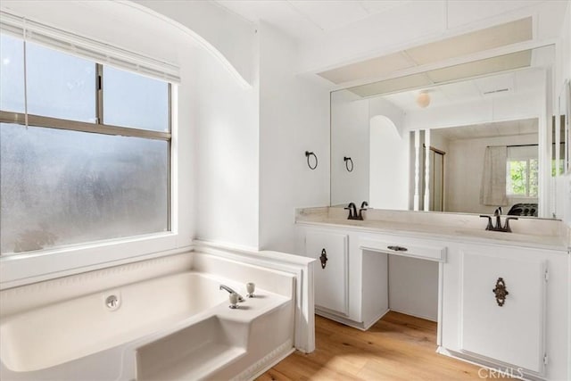 full bath with double vanity, a garden tub, a sink, and wood finished floors