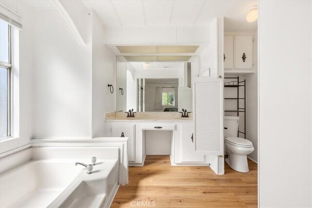 full bathroom featuring toilet, wood finished floors, a wealth of natural light, and a bath