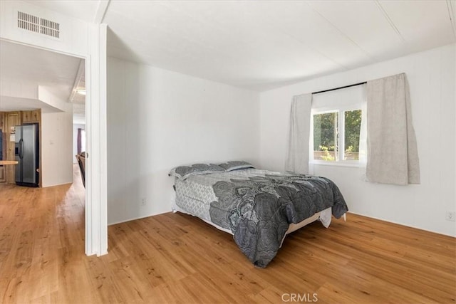 bedroom with stainless steel refrigerator with ice dispenser, visible vents, and light wood-style floors