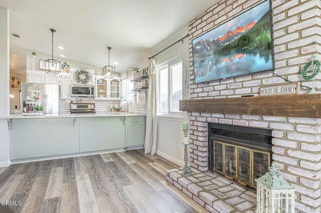 kitchen with white cabinets, appliances with stainless steel finishes, decorative light fixtures, kitchen peninsula, and a brick fireplace