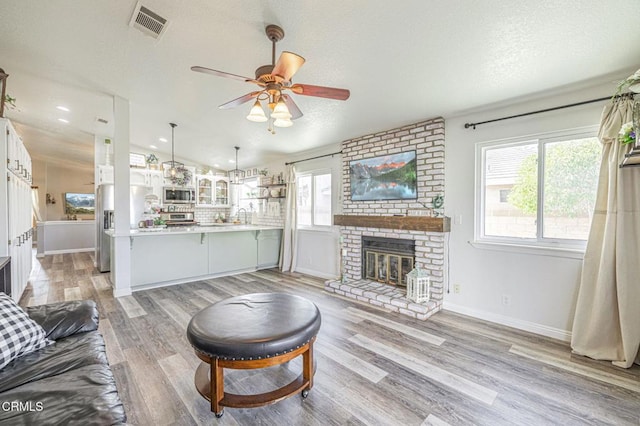 living room with a textured ceiling, light hardwood / wood-style floors, ceiling fan, vaulted ceiling, and a brick fireplace