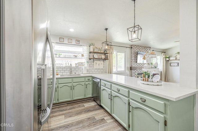 kitchen with kitchen peninsula, appliances with stainless steel finishes, green cabinetry, pendant lighting, and sink