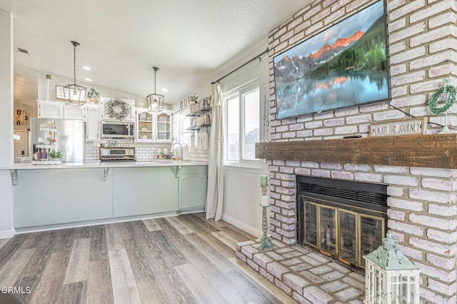 kitchen with wood finished floors, a fireplace, stainless steel appliances, light countertops, and backsplash