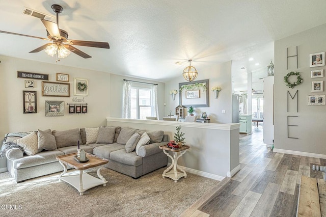 living area featuring visible vents, ceiling fan with notable chandelier, a textured ceiling, wood finished floors, and baseboards