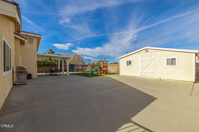 view of patio / terrace with an outbuilding, fence, a storage unit, a playground, and a grill