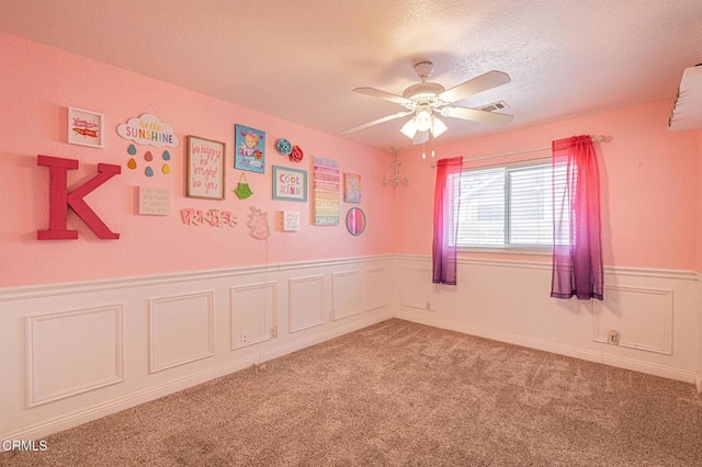 unfurnished room featuring visible vents, a textured ceiling, wainscoting, light colored carpet, and ceiling fan