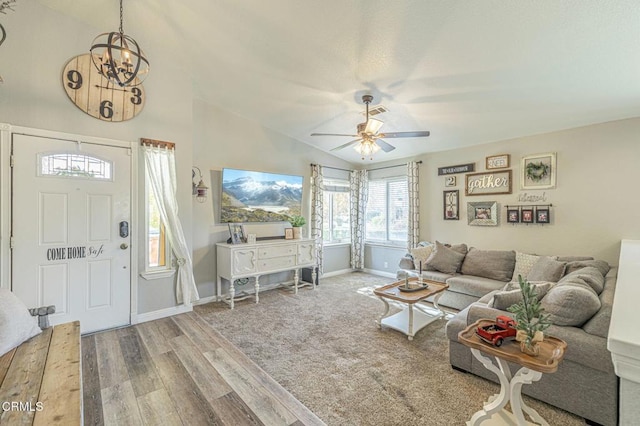 living area featuring ceiling fan with notable chandelier, baseboards, lofted ceiling, and wood finished floors