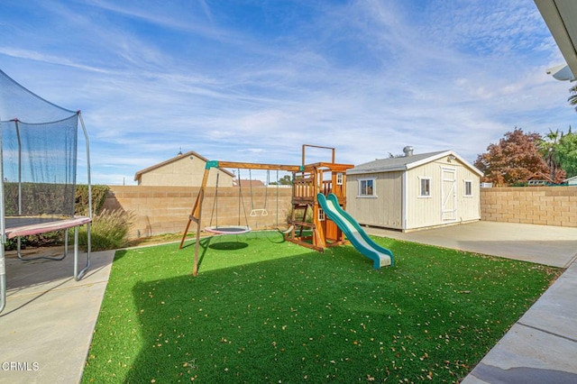 view of jungle gym with a trampoline, a fenced backyard, a yard, an outbuilding, and a storage unit