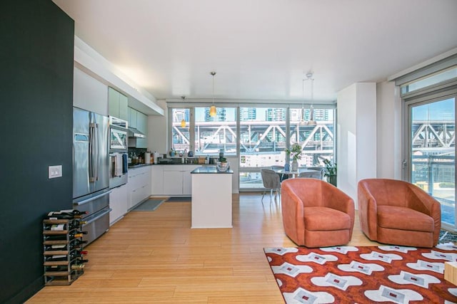 kitchen with stainless steel refrigerator, sink, pendant lighting, light hardwood / wood-style floors, and white cabinets