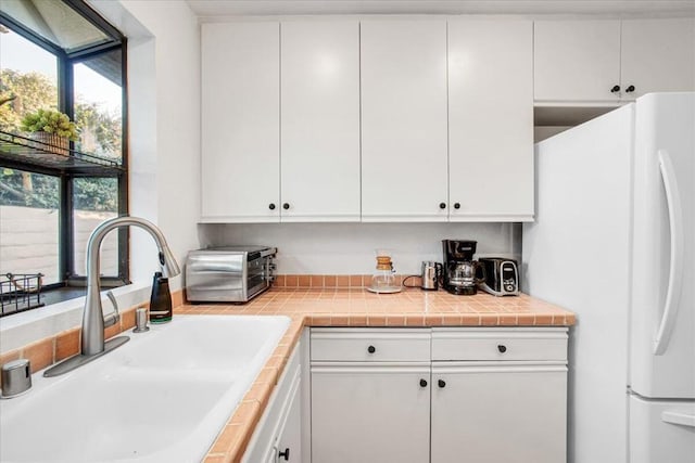 kitchen with white refrigerator, tile countertops, white cabinets, and sink