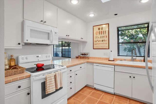 kitchen featuring light tile patterned floors, tile counters, white appliances, white cabinets, and sink