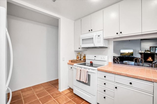 kitchen with light tile patterned floors, tile countertops, white cabinetry, and white appliances