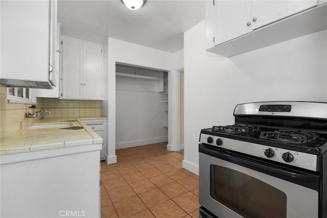 kitchen with light tile patterned floors, stainless steel gas range, tile counters, backsplash, and white cabinets