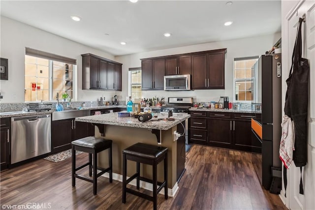 kitchen with appliances with stainless steel finishes, dark hardwood / wood-style floors, a kitchen breakfast bar, light stone counters, and a center island