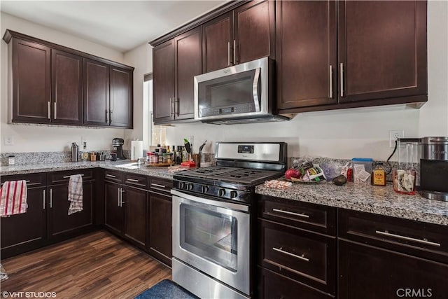 kitchen with light stone counters, dark brown cabinets, dark hardwood / wood-style flooring, and stainless steel appliances