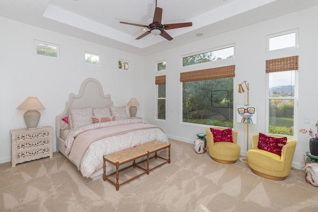 bedroom featuring ceiling fan, light colored carpet, and a raised ceiling