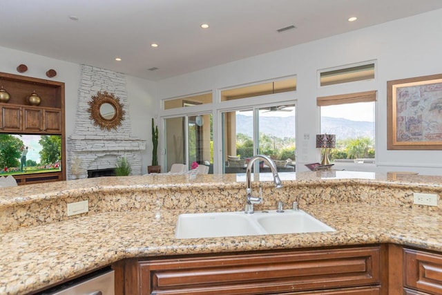 kitchen with light stone countertops, a stone fireplace, sink, a mountain view, and stainless steel dishwasher